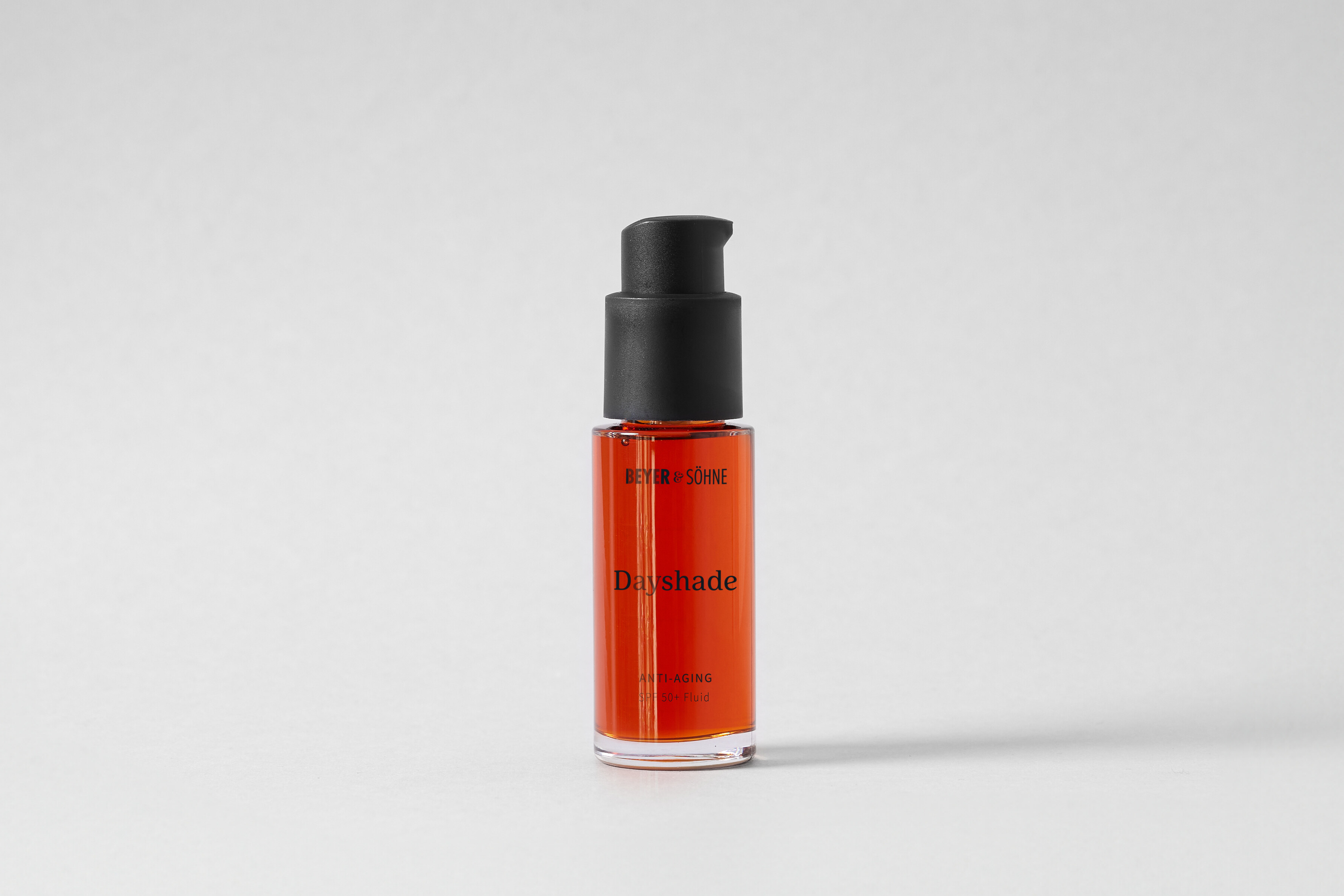 Hochwertiger transparenter Glasspender mit mattem schwarzen Pumpaufsatz und einer roten Flüssigkeit mit der Aufschrift Dayshade Anti-Aging SPF 50 Fluid